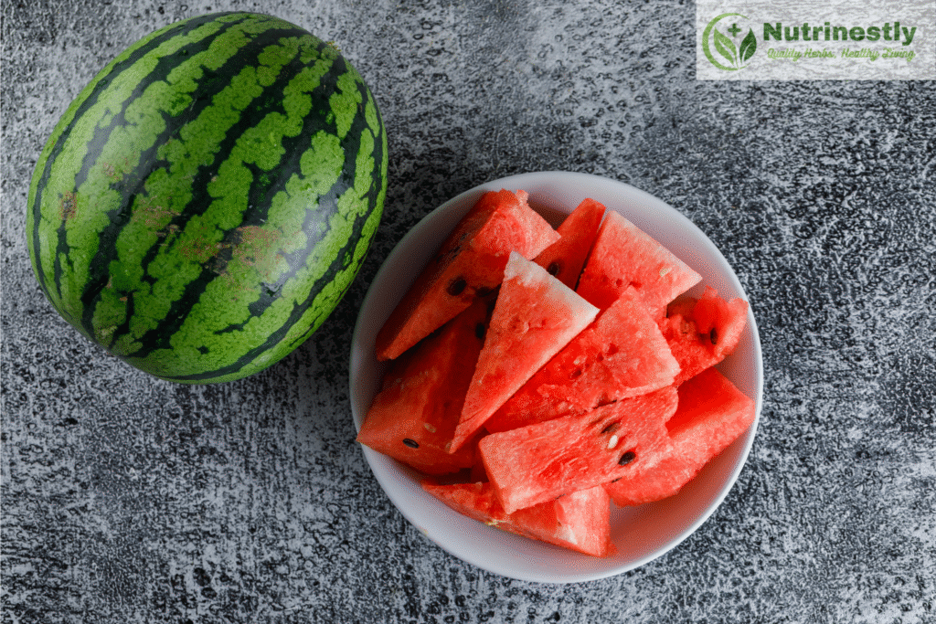 Whole watermelon and a bowl of Watermelon slices on gray grunge background and Nutrinestly website’s logo