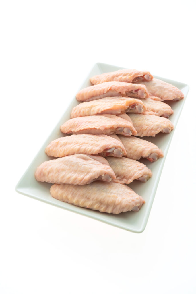 A white rectangular plate filled with raw chicken wings arranged neatly in rows on a white background.