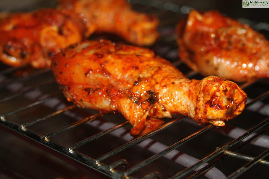 Close-up of marinated chicken thighs grilling on a metal rack, coated in a spicy red seasoning with herbs and spices visible on the surface.