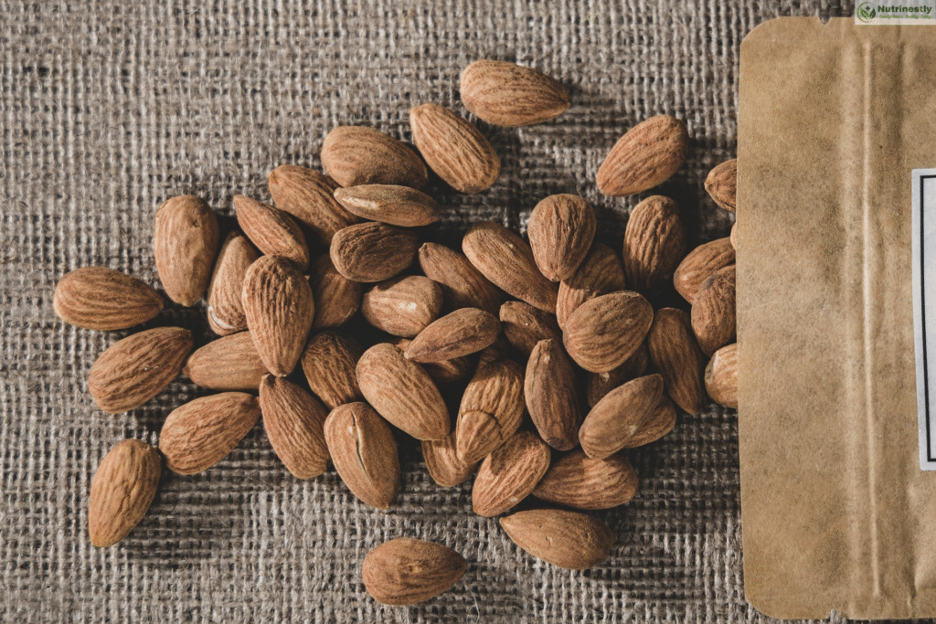 Raw almonds spilling from a kraft paper pouch onto a burlap surface, a nutrient-rich, heart-healthy snack