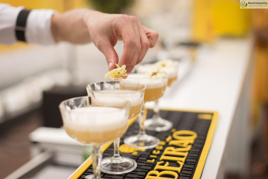 A bartender delicately places a yellow flower garnish on a frothy cocktail in a coupe glass. Several identical drinks are lined up on a bar mat labeled “Licor Beirão.”