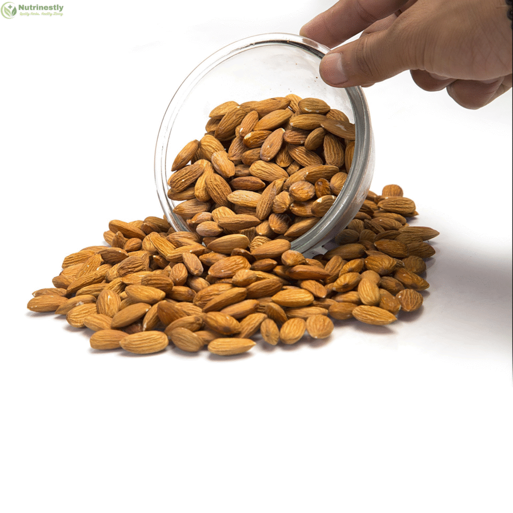 Hand pouring raw almonds from a glass bowl onto a white surface – showcasing a wholesome, nutrient-rich snack