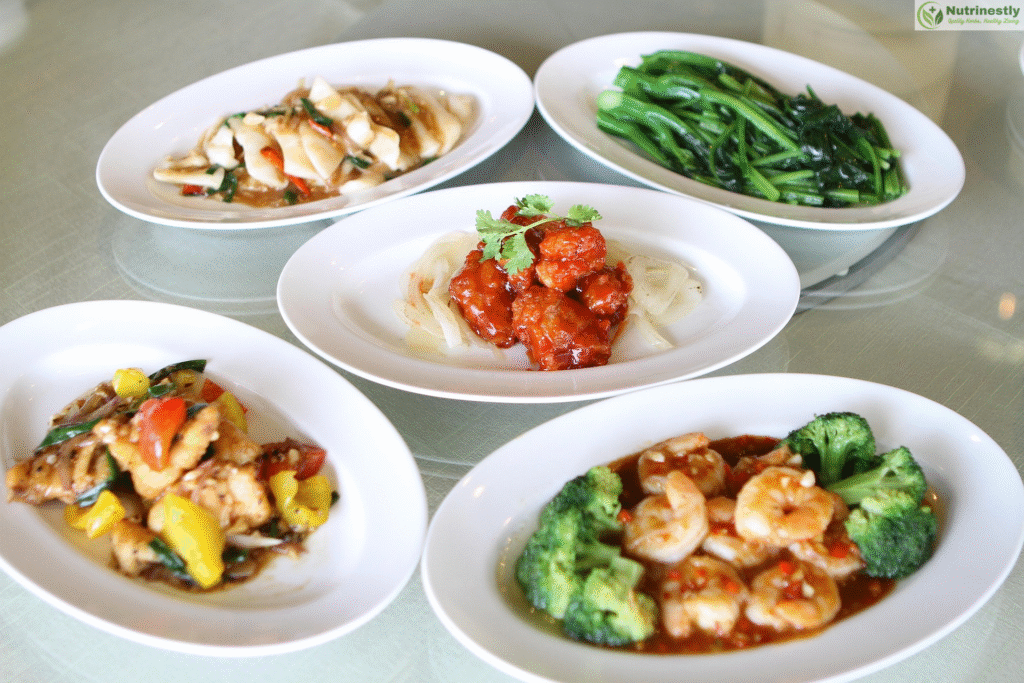 A colorful variety of Chinese food dishes served on white plates, including stir-fried vegetables, shrimp with broccoli, sweet and sour chicken, and sautéed greens showcasing healthy Chinese food options.