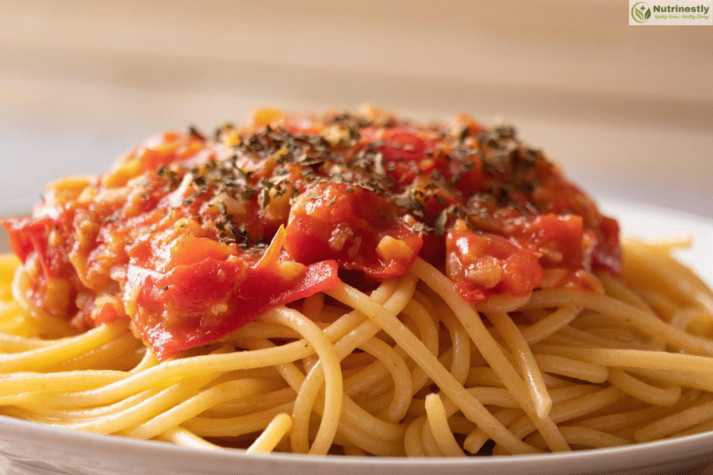 Close-up of freshly cooked spaghetti topped with chunky tomato sauce and sprinkled with dried herbs, served on a white plate.